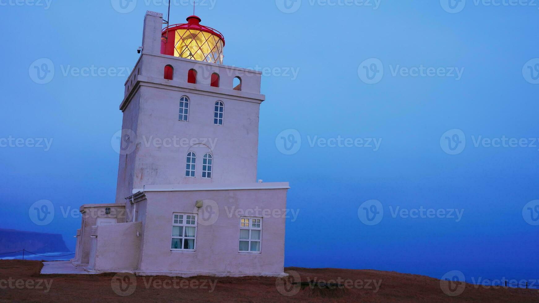 Dyrholaey lighthouse on arctic coastline, beautiful old building with navigation light on shore. Tower structure used for guidance on icelandic cliff, vik city landscapes. Handheld shot. photo