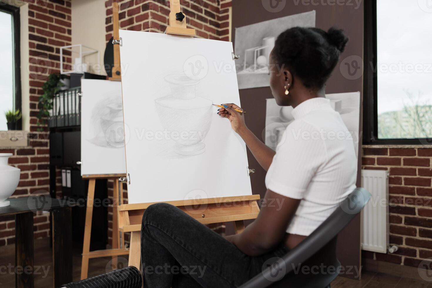 Young African American woman sitting at easel drawing vase on canvas while attending drawing classes, student girl improving sketching skills while studying in art school. Creative hobby concept photo