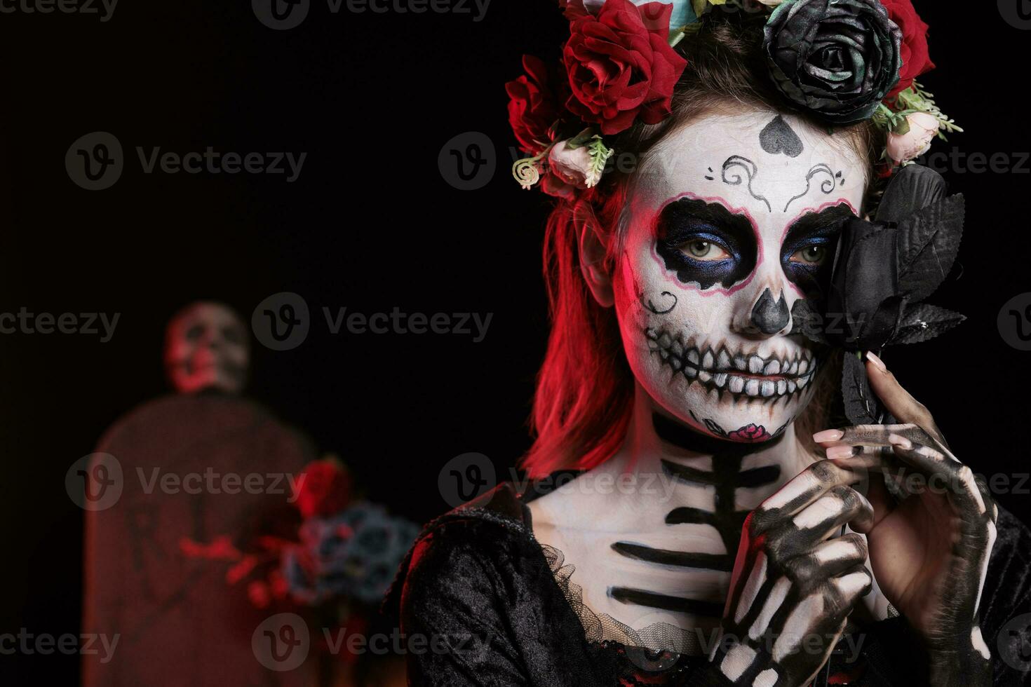 Spooky santa muerte lady posing with black roses, acting like holy goddess of death on day of the dead mexican holiday. Celebrating halloween ritual with la cavalera catrina skull body art. photo