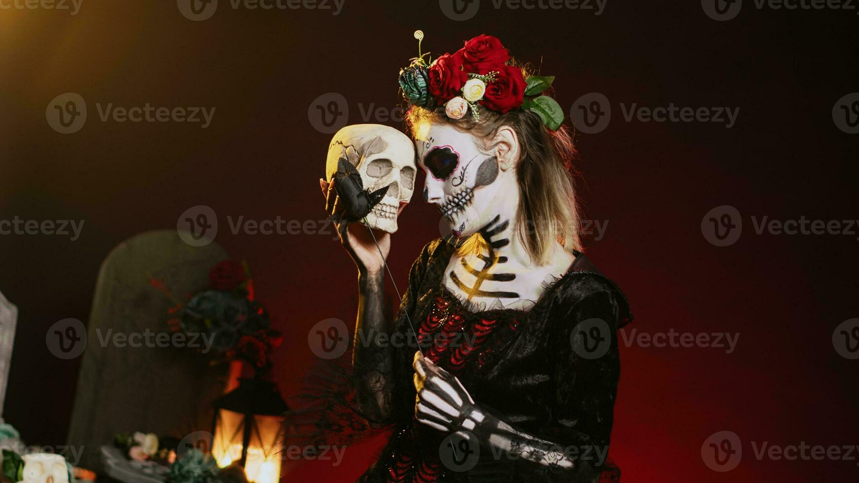 Glamorous woman acting creepy with skull in hand, holding black roses and wearing scary make up. Looking like santa muerte with body art on holy mexican celebration, being flirty. Handheld shot. photo