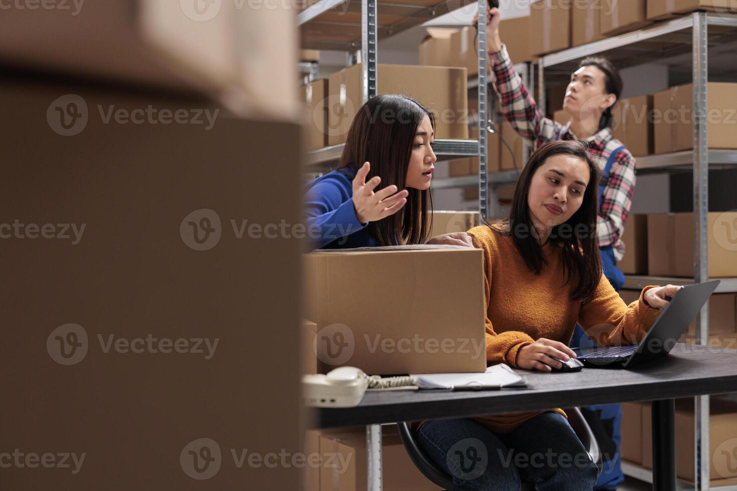 Storehouse employees checking customer delivery satisfaction on laptop and arguing about negative feedback. Postal service asian women coworkers managing shipment from warehouse computer photo