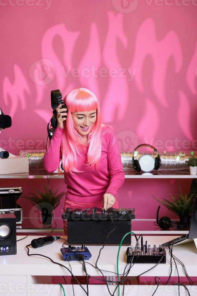 Artist mixing techno song at professional turntables listening music with headphone while doing performance in club during nighttime. Asian woman recording album using audio equipment photo