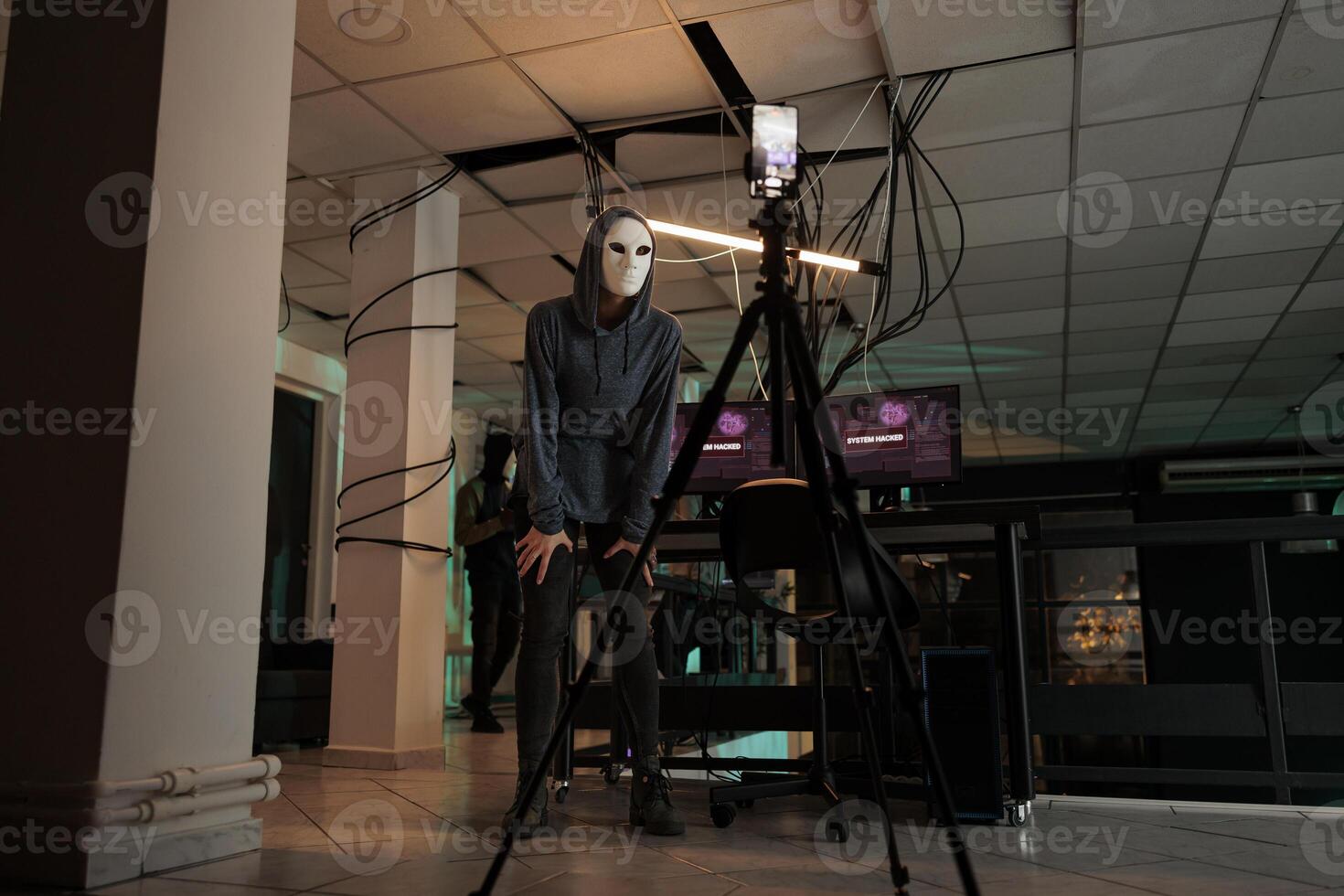 Online cybercriminal in anonymous mask recording live video, threatening to expose government data on camera. Young hacker stealing personal information and asking ransomware, cyberattack. photo