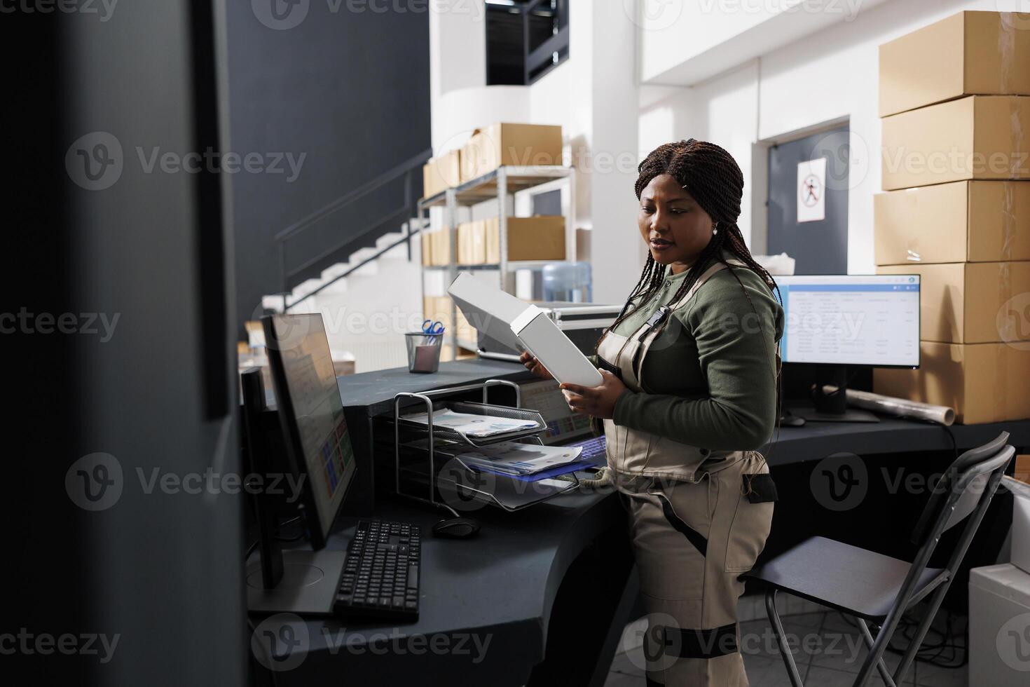 African american storehouse employee holding white boxes, preparing customers orders for shipping in storage room. Stockroom worker checking products logistics during goods inventory photo
