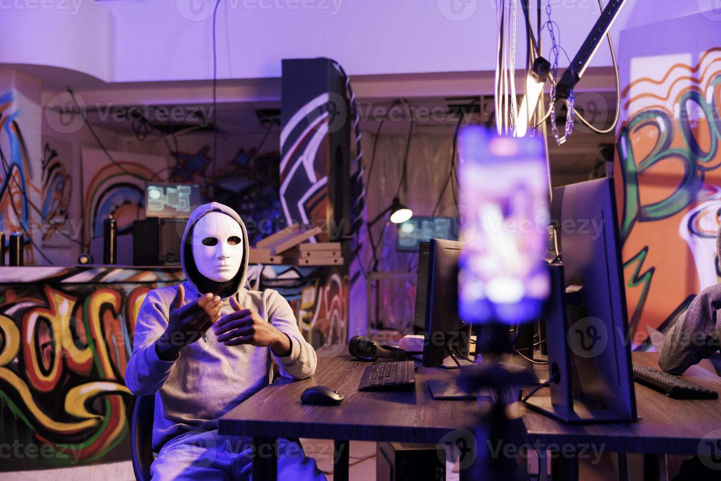 Anonymous scammer threatening online on mobile phone while planning internet fraud. Criminal recording ransom video on smartphone while doing crime in abandoned warehouse photo