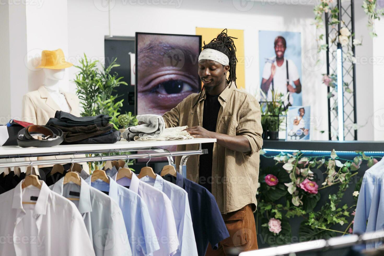 Smiling young african american man choosing casual apparel in shopping mall clothing store. Customer standing near rack with shirts and searching garment while checking size photo