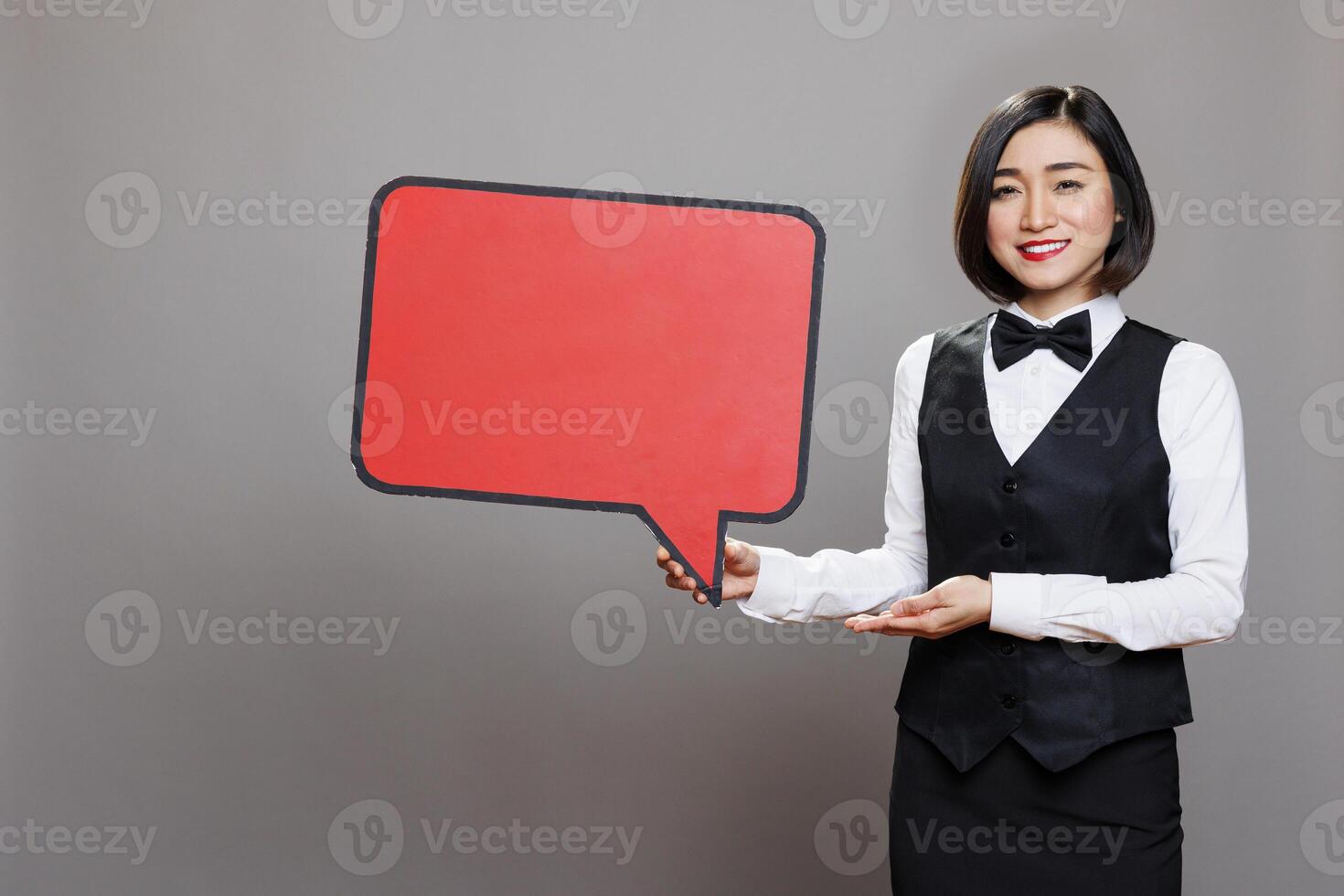 Asian waitress wearing professional uniform showing red blank speak frame studio portrait. Restaurant smiling woman worker holding empty chat bubble mockup and looking at camera photo