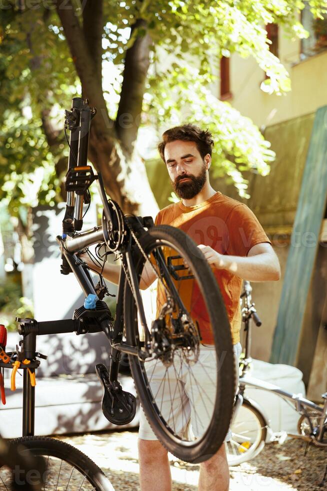 Image showcasing committed healthy athletic man meticulously inspecting modern bicycle for regular summer maintenance. Active young caucasian male carefully grasping bike components for repair. photo