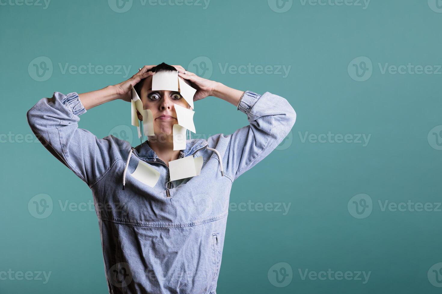 Exhausted unhappy woman writes down memo messages using paper sticky notes, helping her with plenty details about work. Colorful memory reminder on tired depressed young adult, studio shot photo