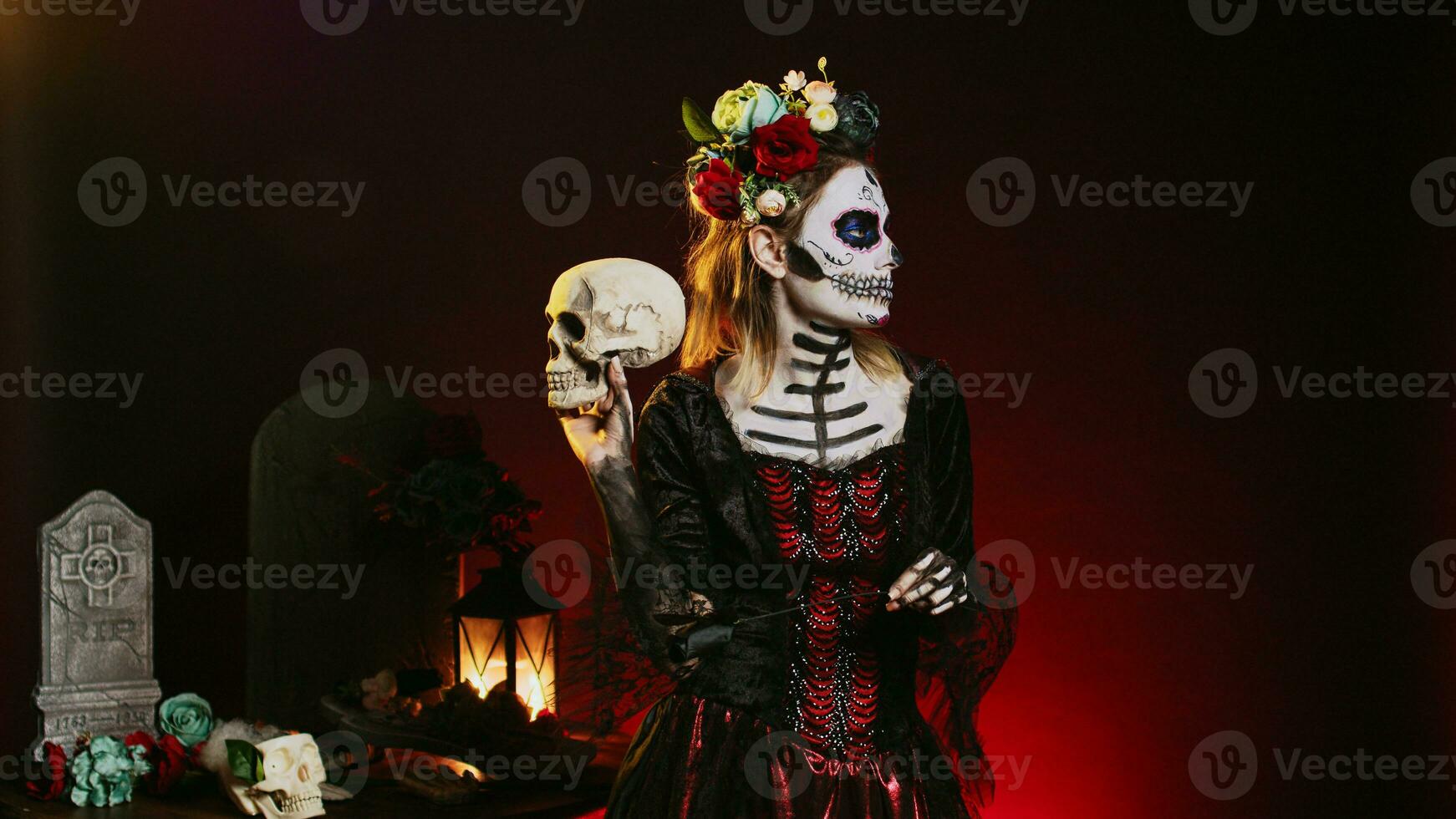 Horror scary model wearing traditional make up to celebrate mexican holiday, holding skull in studio. Looking like santa muerte or goddess of death on holy dios de los muertos celebration. photo