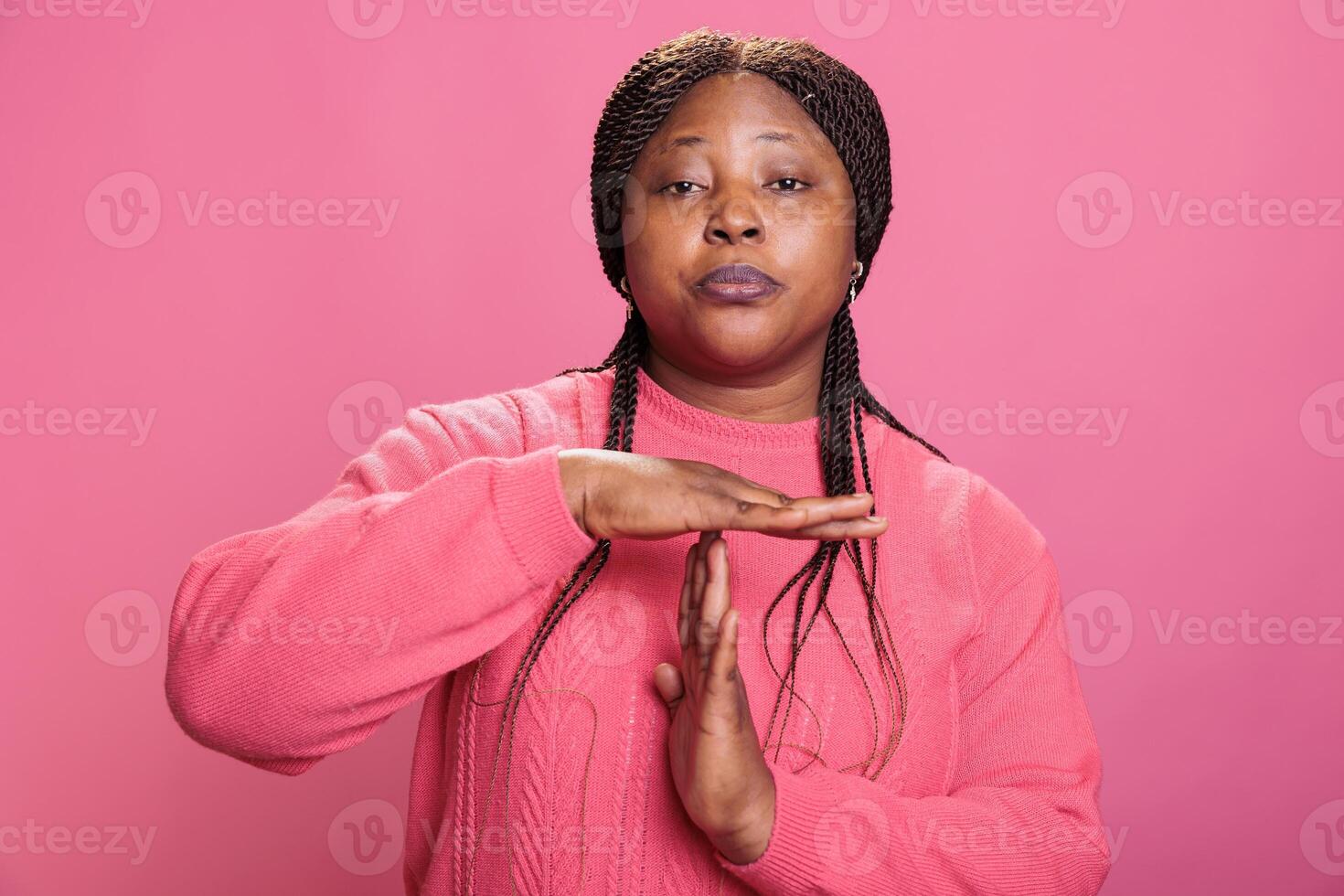 Angry woman doing timeout gesture with t shape hands making break time sign with arms in studio with pink background. African american young adult advertising pause symbol with palms photo