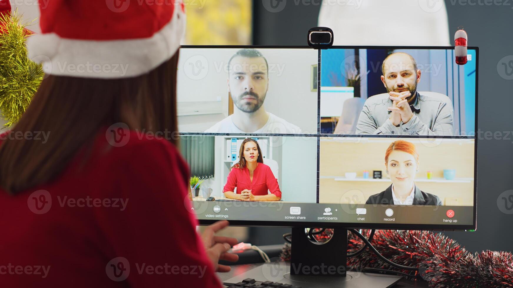 Close up shot on computer screen showing team meeting in online videocall in Christmas decorated office. Employee wearing Santa hat chatting with coworkers in teleconference photo