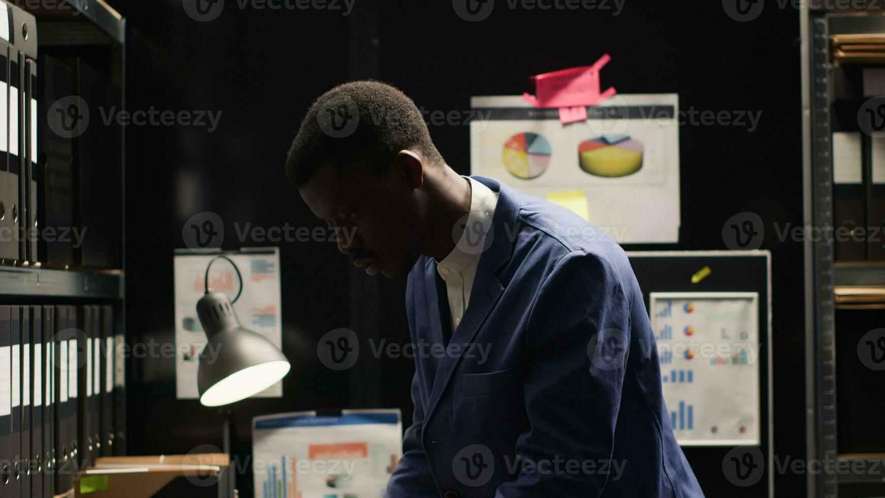 Private investigator stands and walks out of the office while carrying laptop bag. African american policeman closes his personal computer and arranges workstation, leaving for the day. photo