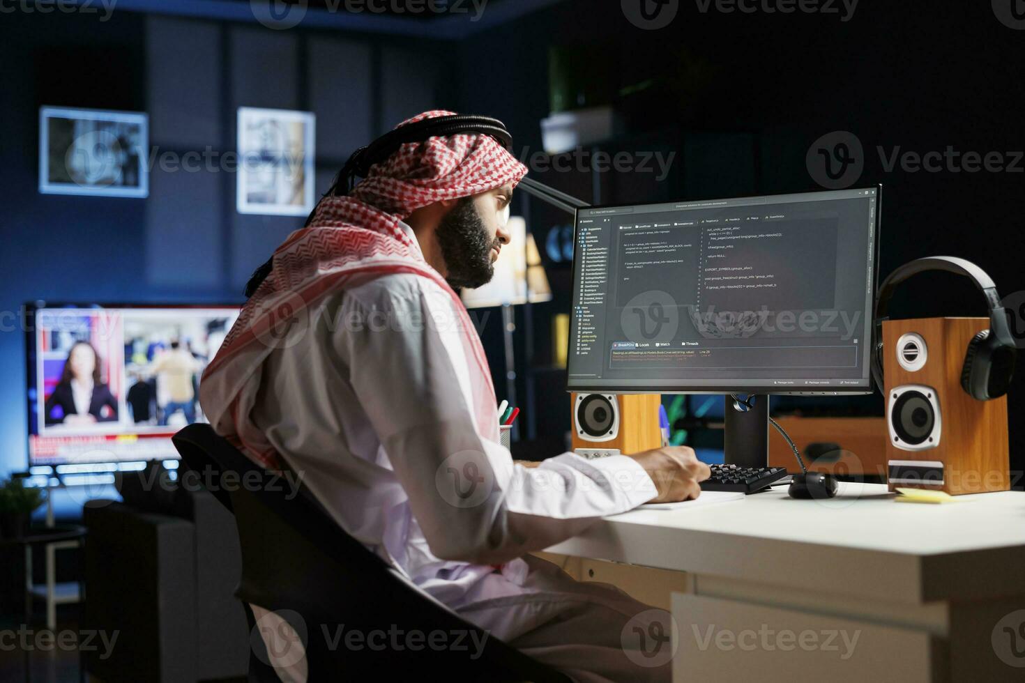 dedicado software programador vistiendo tradicional Arábica ropa es sentado a su hogar oficina escritorio examinando base de datos código en computadora. musulmán hombre comprobación el programación idioma en el ordenador personal monitor. foto