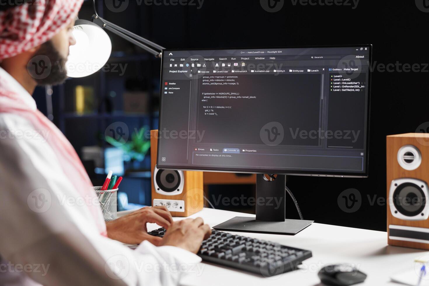 Muslim man sitting at desk and coding on computer, showcasing process of app development. Selective focus on pc monitor displaying running algorithms compiled by Arab guy in traditional attire. photo