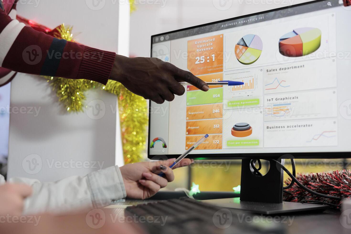 African american employee in Christmas decorated office showing colleagues key data point on computer screen. Company team working together on finishing project before incoming deadline photo