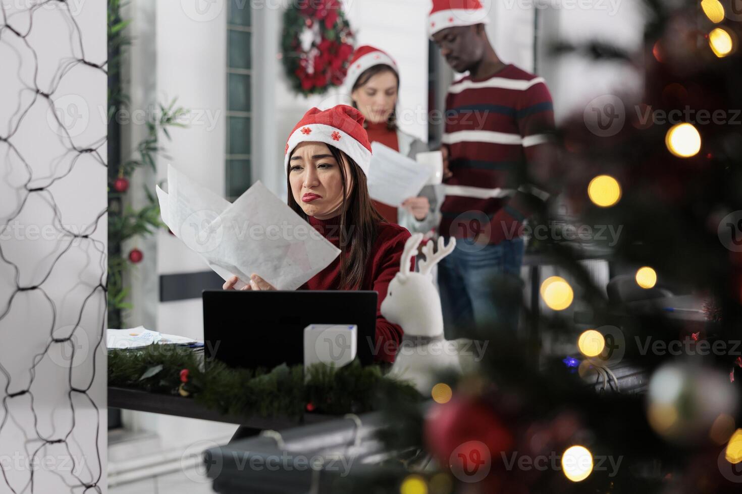 Depressed workaholic employee upset by stressful company paperwork overdue on Christmas. Stressed employee getting overworked in festive decorated workplace, trying to finish tough project photo