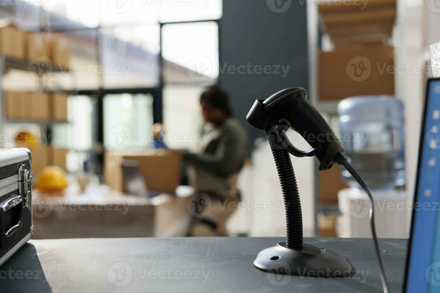 Selective focus of store scanner standing on counter desk in warehouse, in background african american employee preparing packages for delivery. Stockroom supervisor working at customers online orders photo