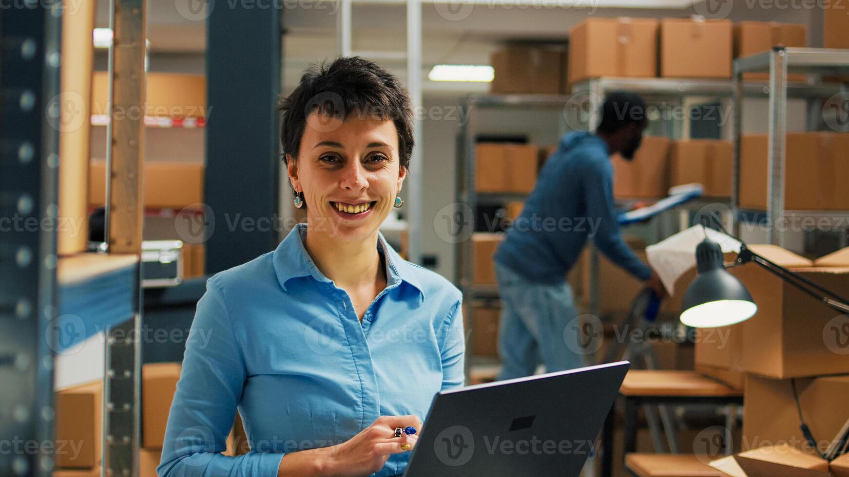 Female worker checking cardboard packages from storage room racks, using laptop to plan stock inventory and take notes. Entrepreneur working on business development and supply chain. photo