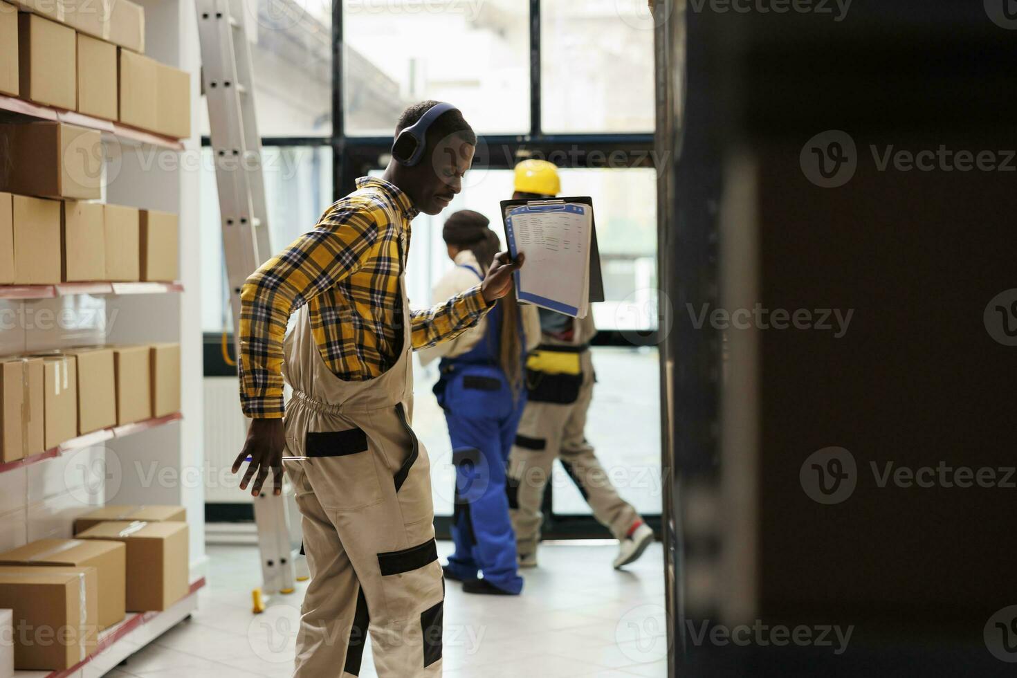Warehouse supervisor holding papers clipboard and dancing in stockroom. African american storehouse operative wearing heapdones, listening to music and making movements at work photo