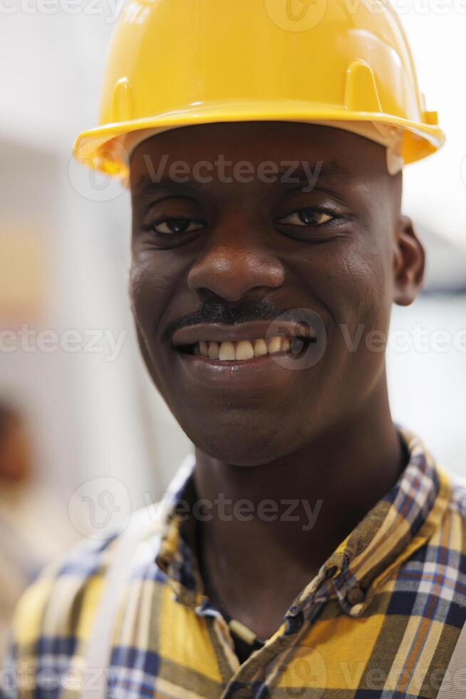 African american warehouse worker wearing safety helmet face portrait. Smiling storehouse loader with happy facial expression in industrial protective equipment looking at camera close up photo