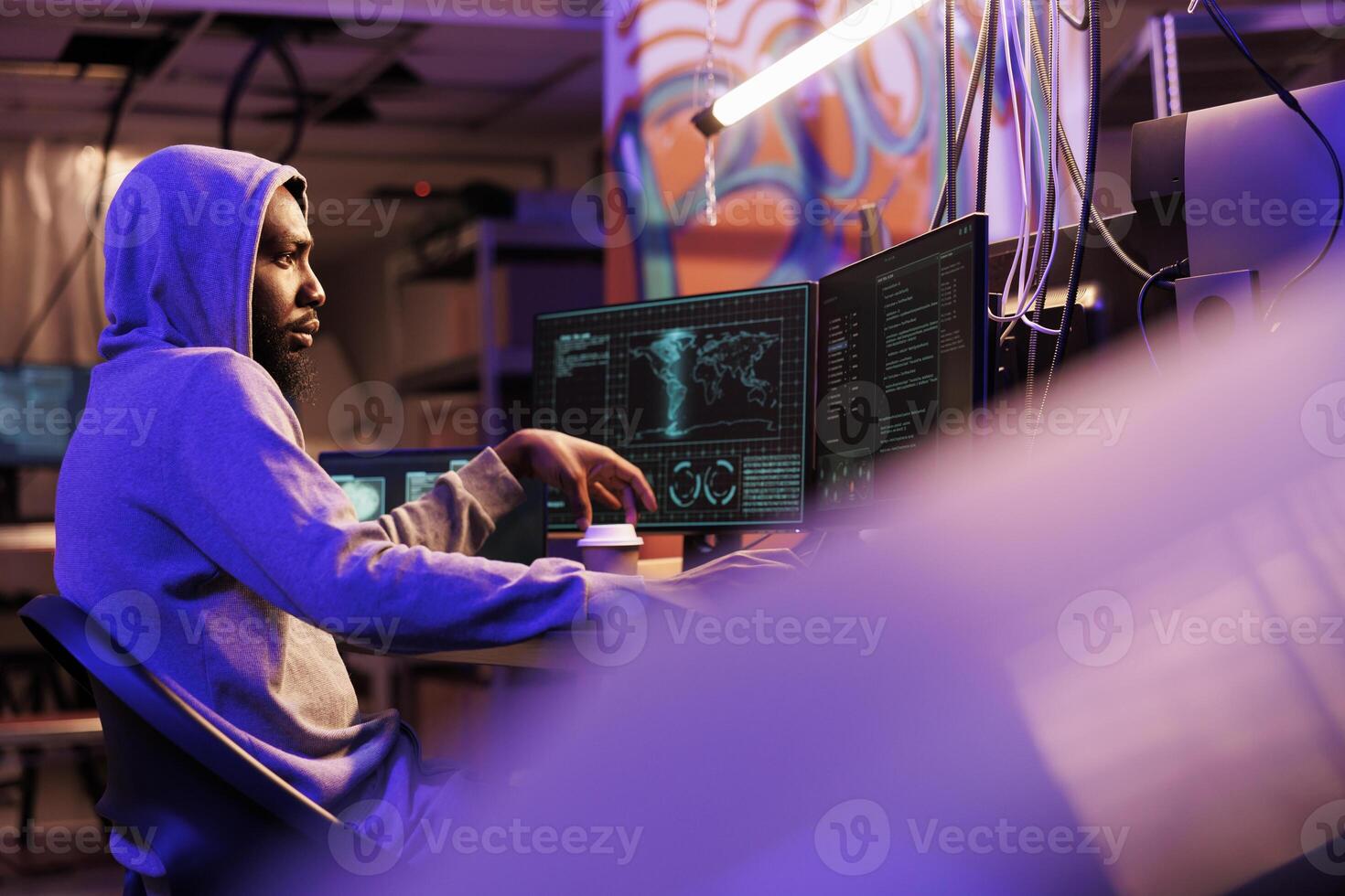 Hacker running malicious spyware on computer and checking confidential information on screen while drinking coffee. Man in hood using malware and doing illegal activities photo