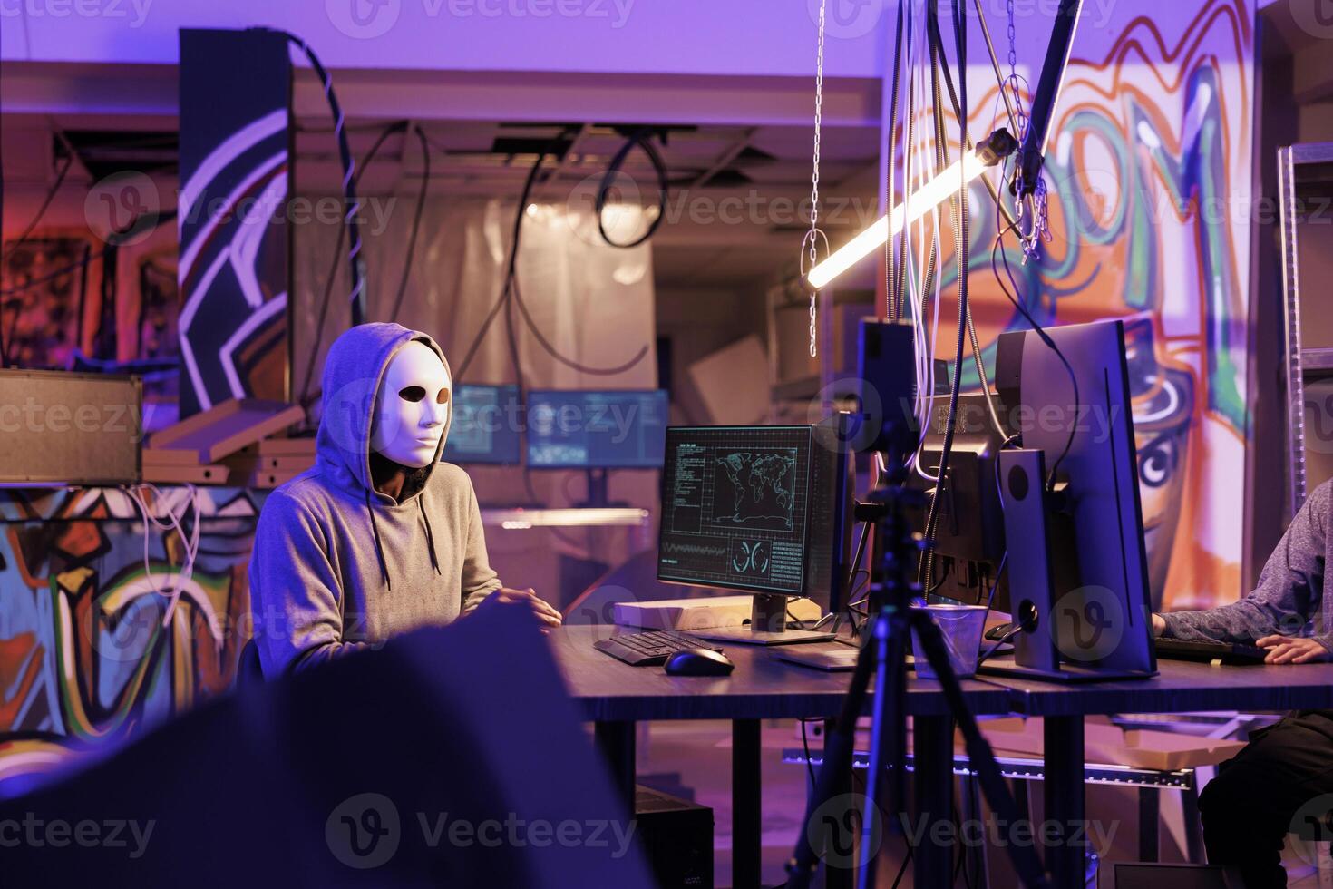 Internet thief streaming threat on smartphone and demanding money on dark web. Criminal in anonymous mask recording harassment and ransom video on mobile phone late at night photo