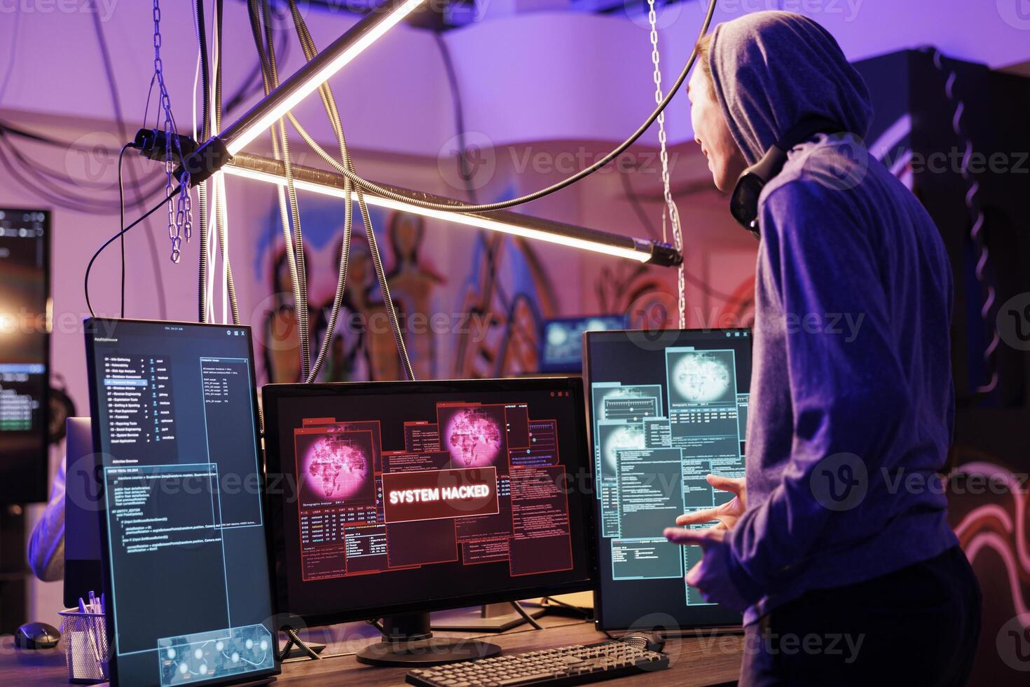 Happy hacker successfully breaking into website using malicious software. Cheerful smiling criminal in hood hacking computer network system in abandoned warehouse at night photo