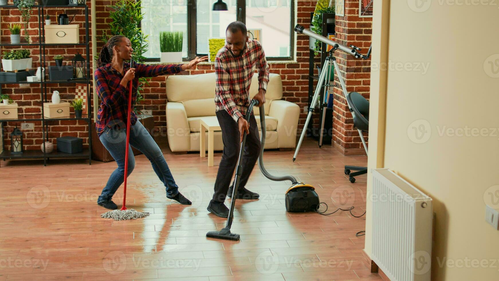 Young happy couple listening to music and washing floors in apartment, doing silly dance moves. Cheerful people doing spring cleaning and dancing, mopping tiles. Handheld shot. photo