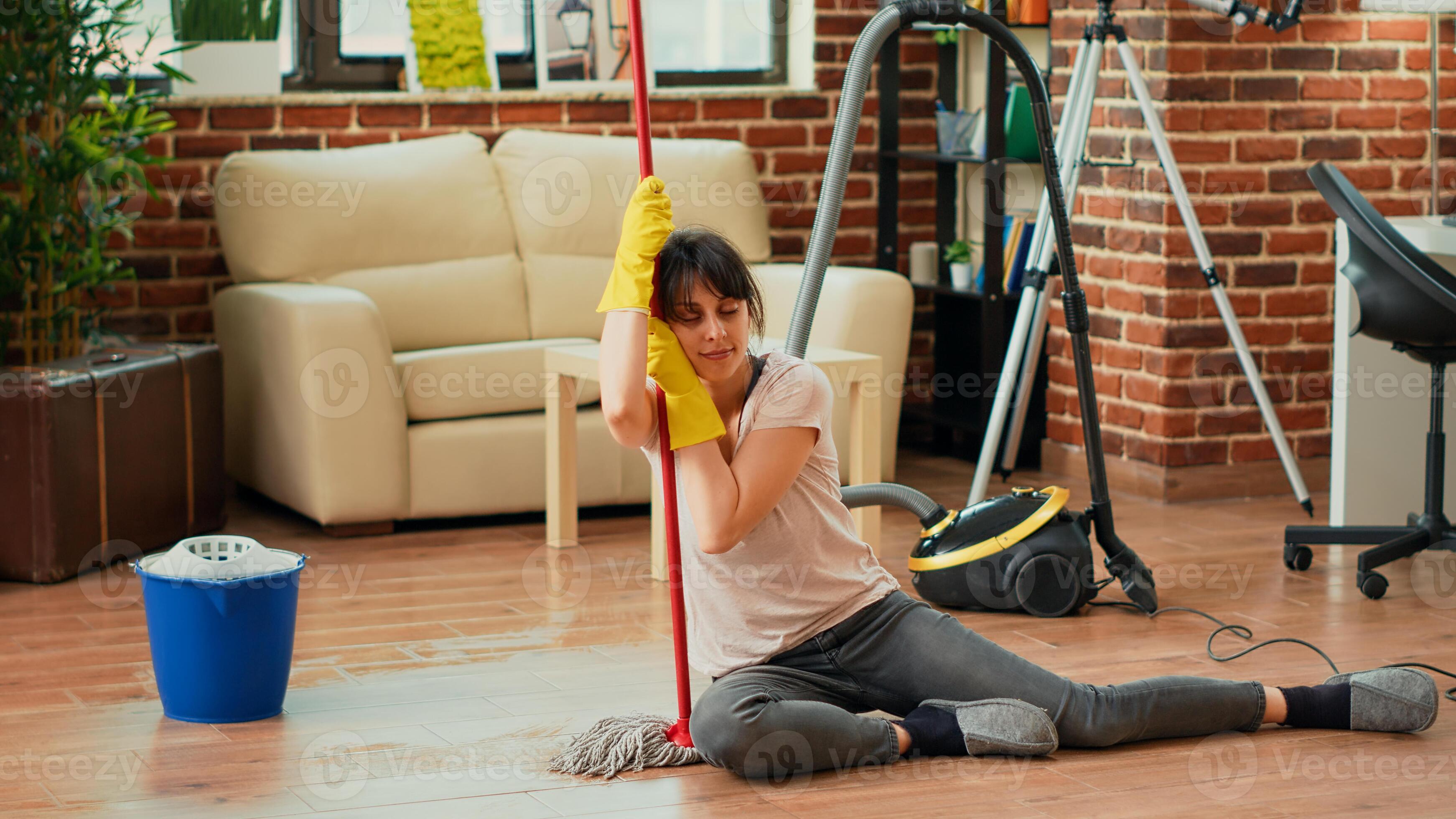 Exhausted woman sitting on living room floors with mop and bucket