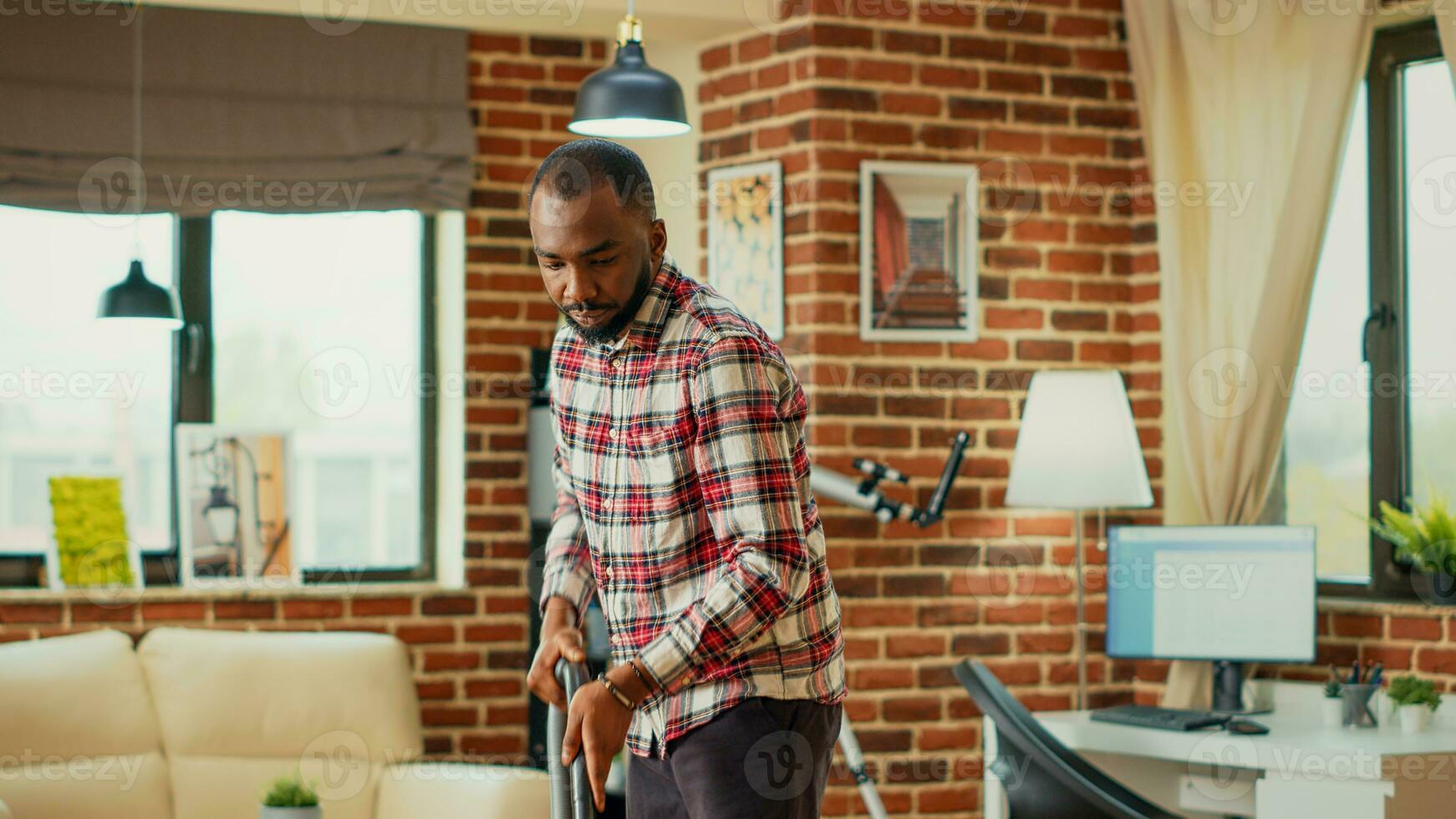 Modern male person doing spring cleaning session at home, using vacuum cleaner to clean up apartment. Young cheerful man vacuuming wooden living room floors, using washing solution. photo