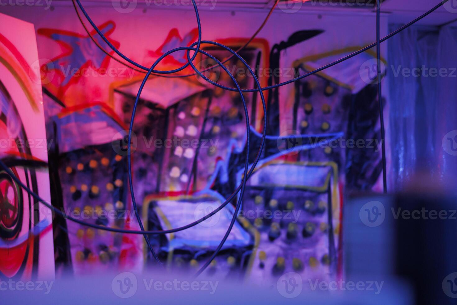 Crumbling structure covered in dust glowing in the dark, messy walls with spray paint being illuminated by bright neon lights. Abandoned old building with garbage and fluorescent purple lights. photo