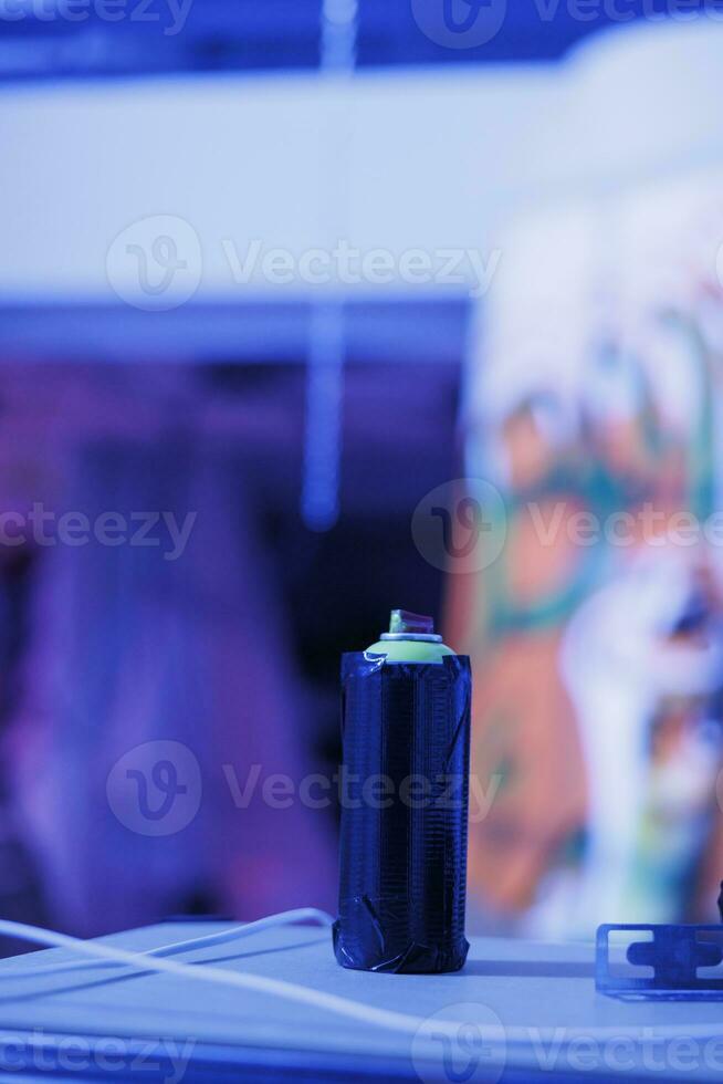 Aerosols bottles used for graffiti art on neglected walls, spray paint cans in deserted warehouse with purple bright lights. Damaged empty building with fluorescent neon lights. Close up. photo