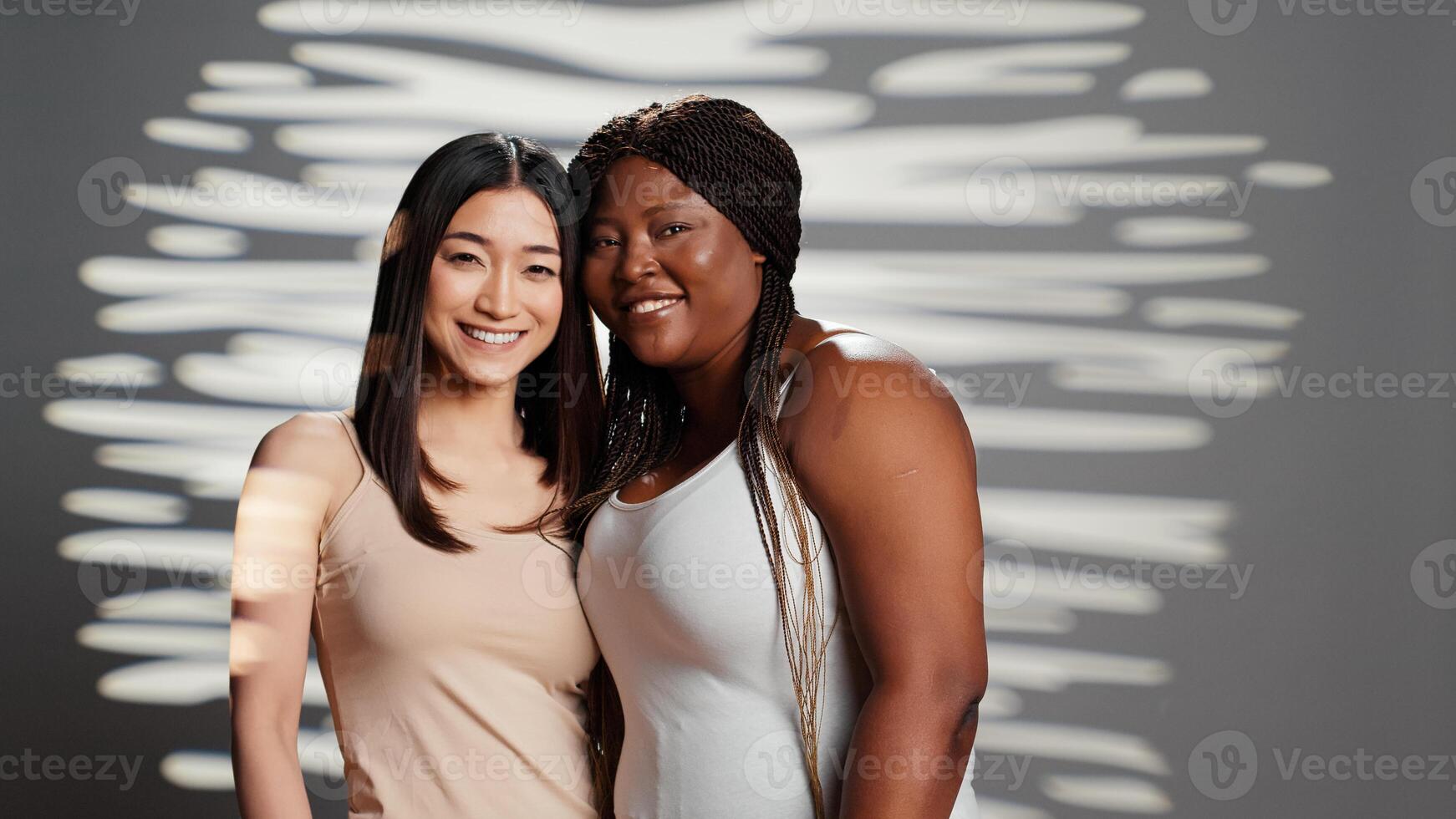 Flawless confident diverse girls posing together on camera, showing self confidence and body positivity. Two beautiful skincare models hugging and promoting different bodies and skintones. photo