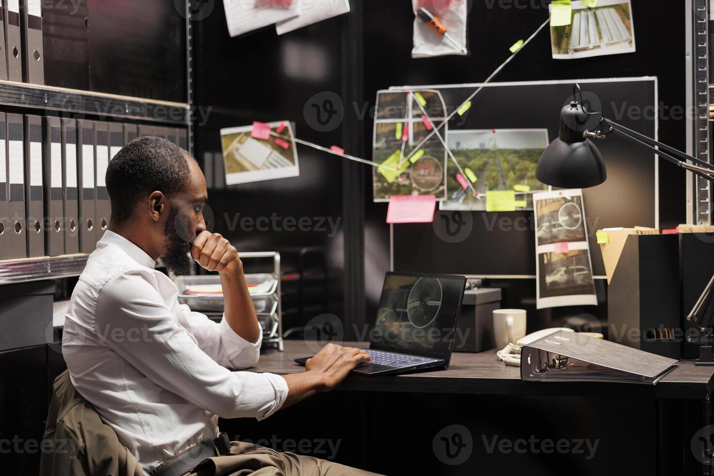 Private detective wathing cctv camera photos on laptop while sitting at workplace desk. African american investigator analyzing surveillance photographs on computer screen