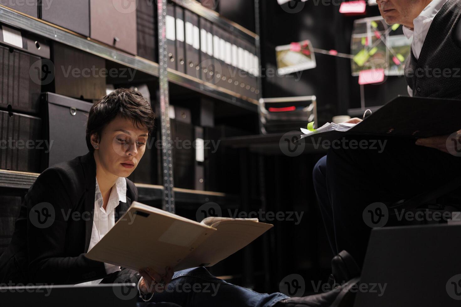 Tired investigator holding files with crime scene evidence, analyzing criminology department report in arhive room. Overworked private detectives working overhours at missing person case photo