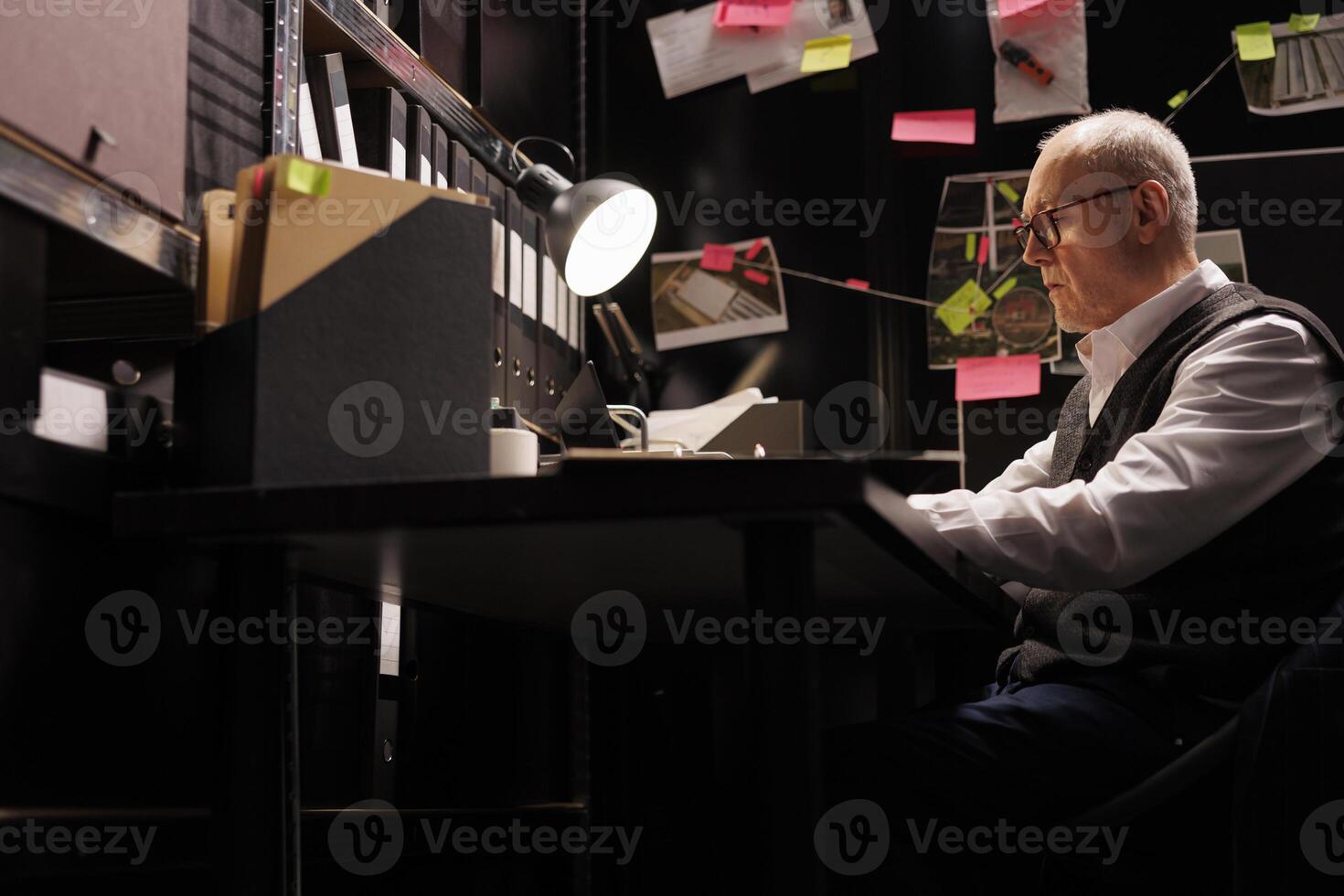 Senior police officer analyzing federal documents, working overtime at criminal case in arhive room. Elderly private detective analyzing mysterious suspect report, checking victim files photo