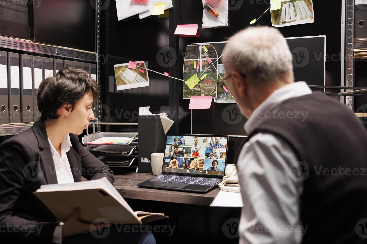 Private detectives having online videocall with remote team, discussing mysterious suspect report, working late at night at criminal case in arhive room. Meeting conference on laptop computer photo