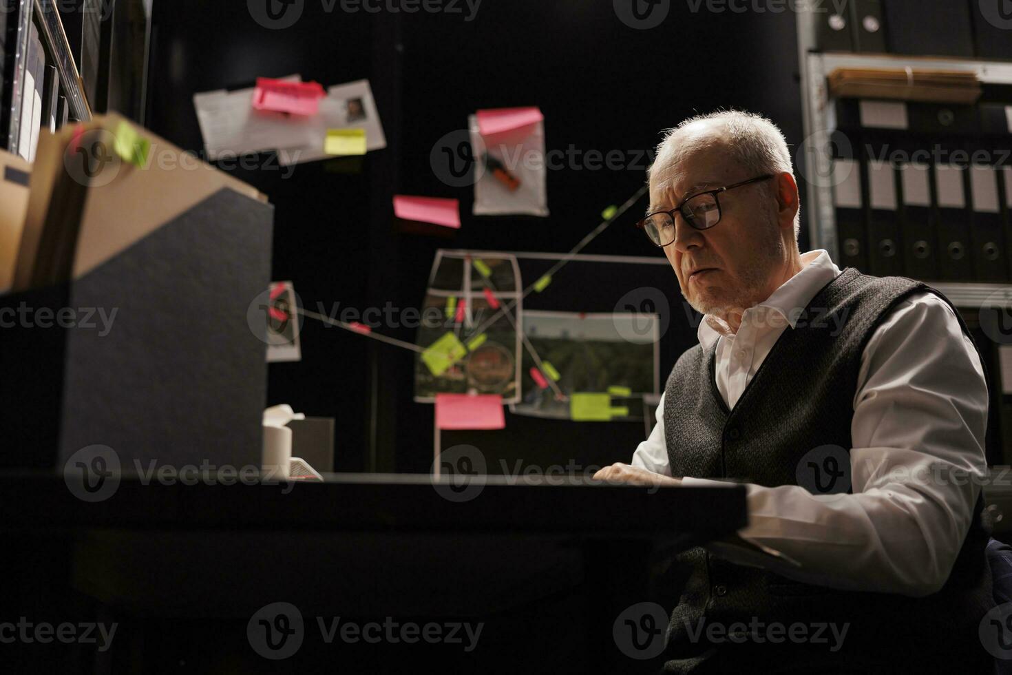 Overworked senior police officer working overhours in arhive room, analyzing criminal case evidence. Tired private detective sitting at desk checking mysterious suspect report. Investigation concept photo