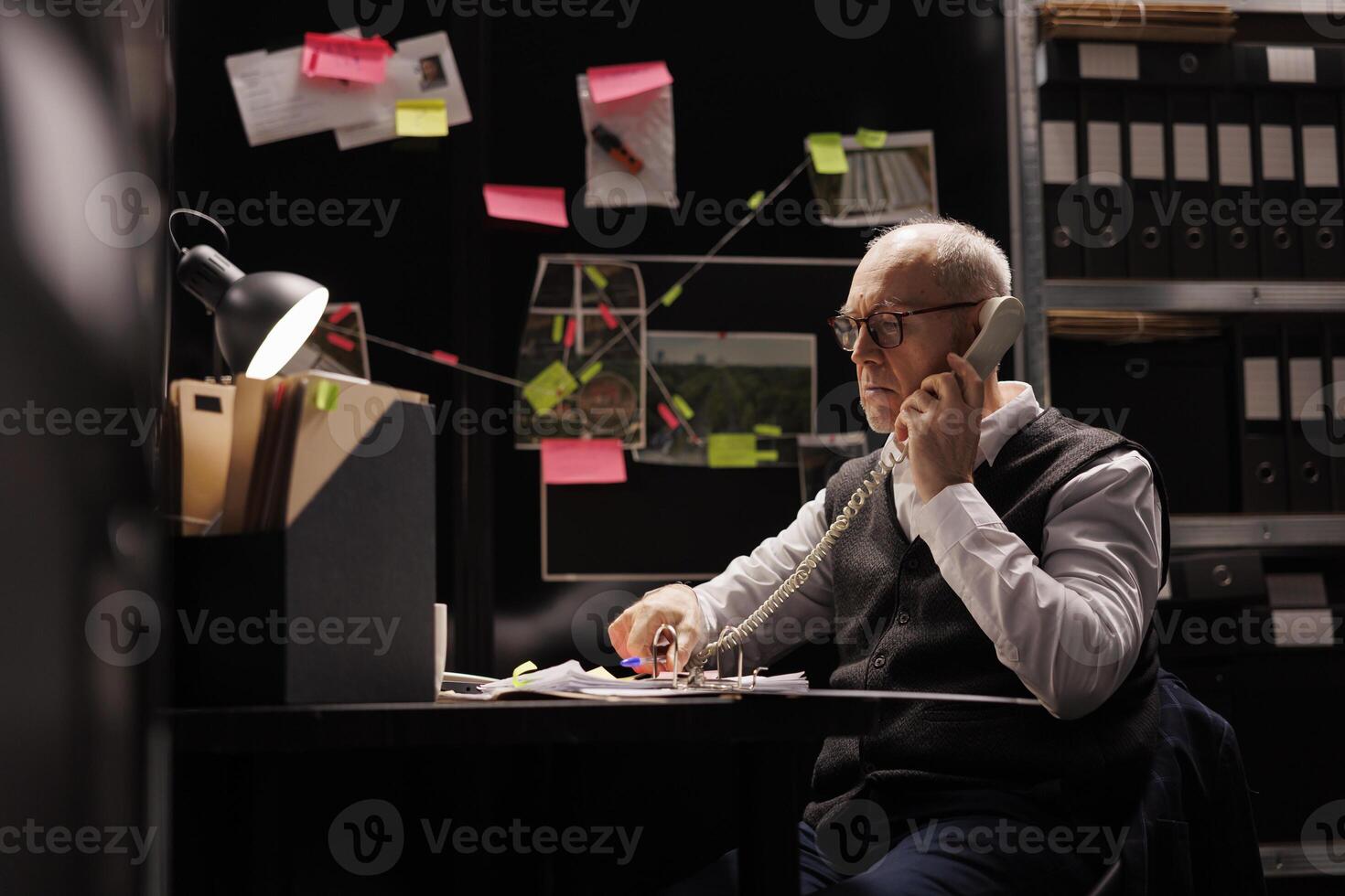 Police officer talking at landline phone with remote inspector, discussing criminal investigations case. Elderly private detective working overtime at crime scene report, analyzing evidence photo