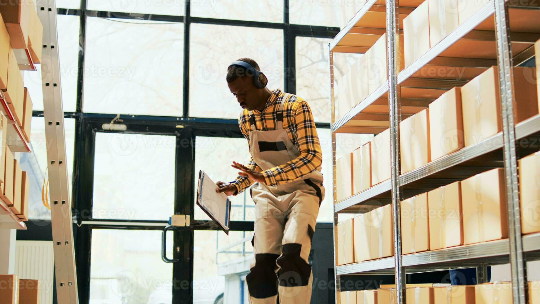 Male worker showing dance moves in warehouse space, working in depot with containers of retail products. Young man having fun singing dancing in storage room, manufacturing industry. Handheld shot. photo