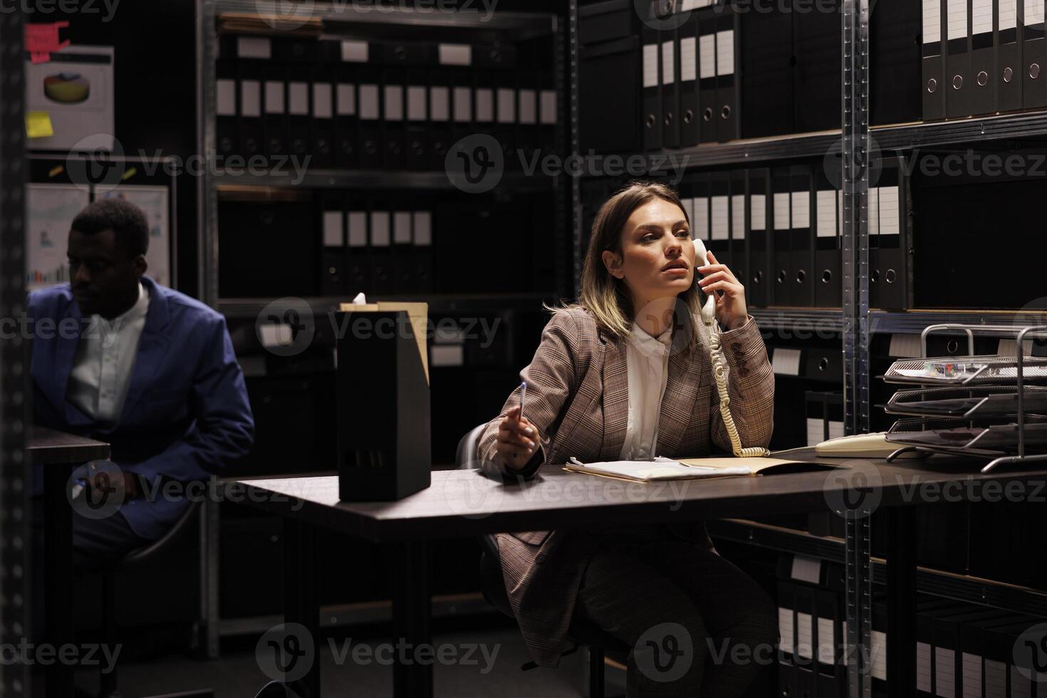 Manager having remote talk with businessman, working overtime at accountancy report arhive room. Confident repository employee organizing administrative files, searching for management research photo