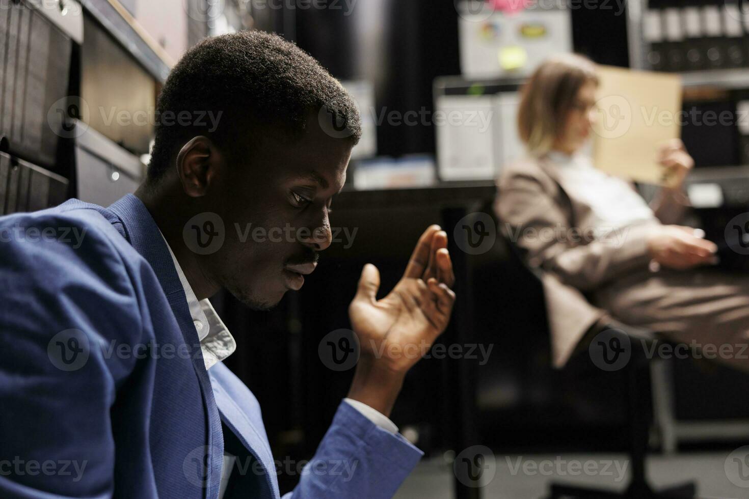 Tired diverse colleagues working overtime in arhive room, analyzing criminal case evidence. African american private detectives checking crime scene footage trying to catch mysterious suspect photo