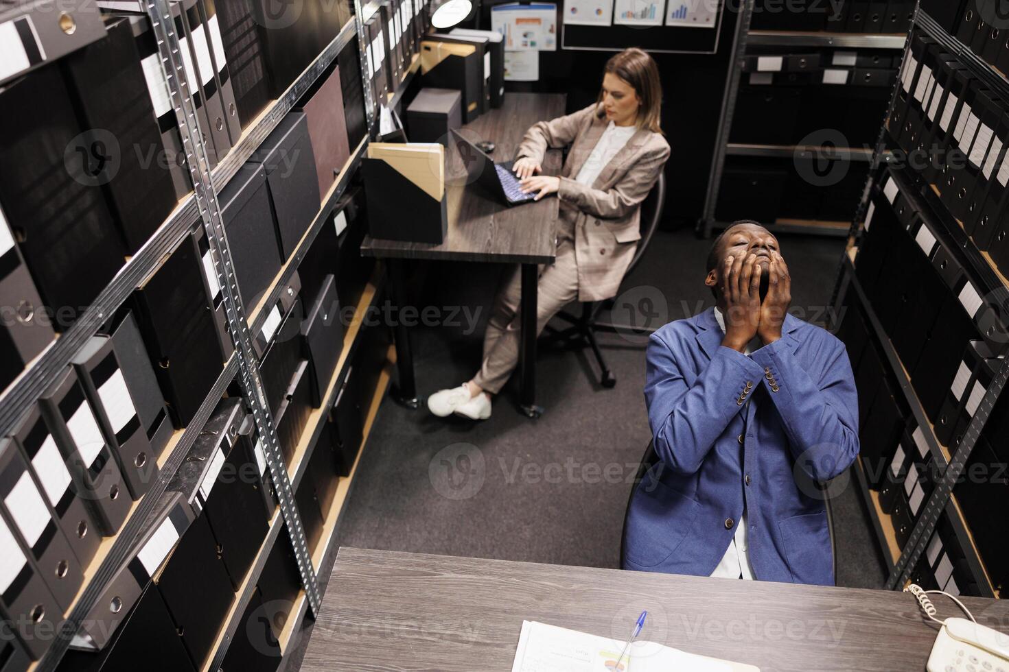 Top view of manager with thoughtful expression, brainstorming ideas to solve bureaucracy report in storage room. Diverse business people working overtime at administrative research photo