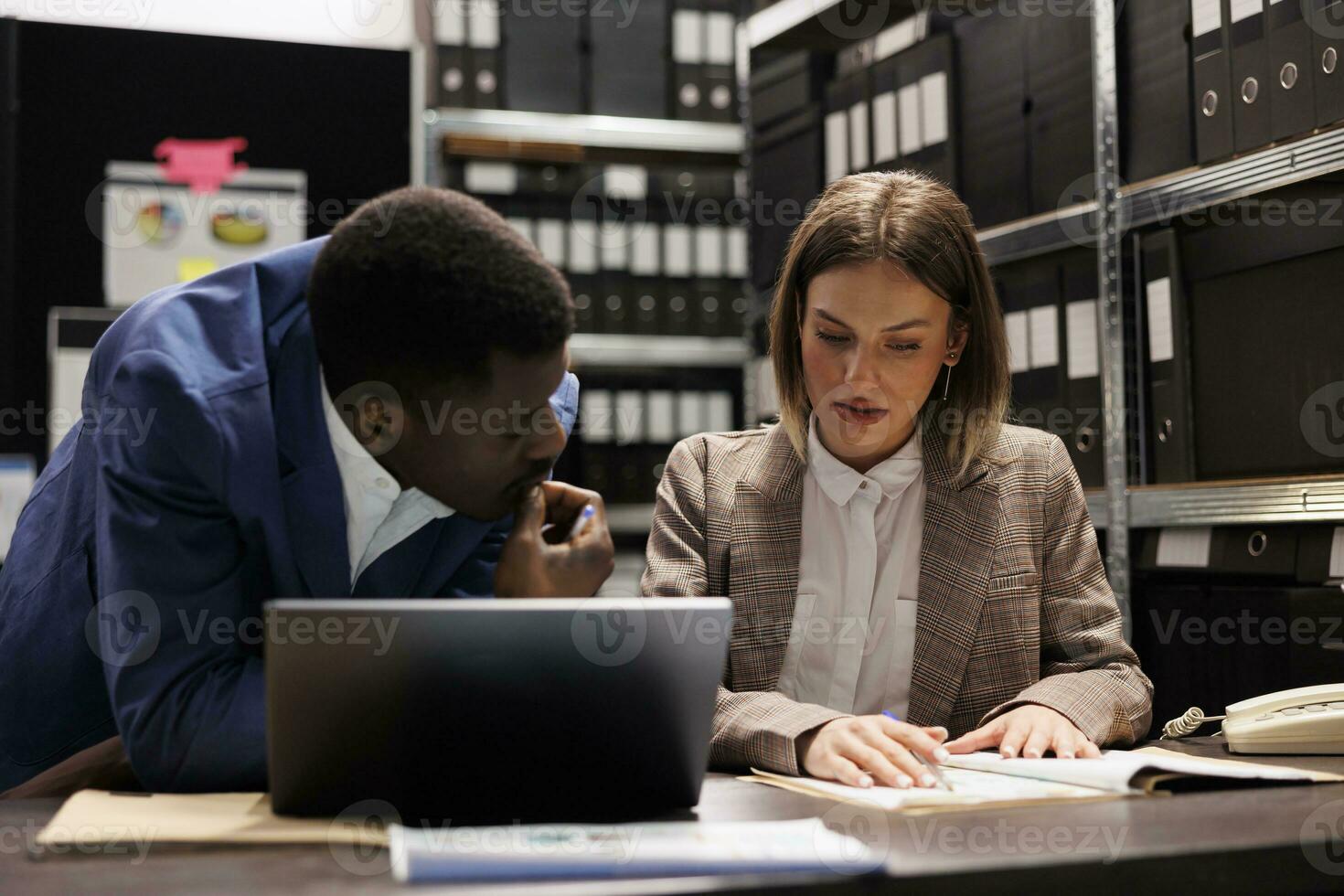 Businesspeople managing financial documentation, analyzing corporate administrative documents. Diverse managers discussing bookkeeping report in storage room, organizing business files photo