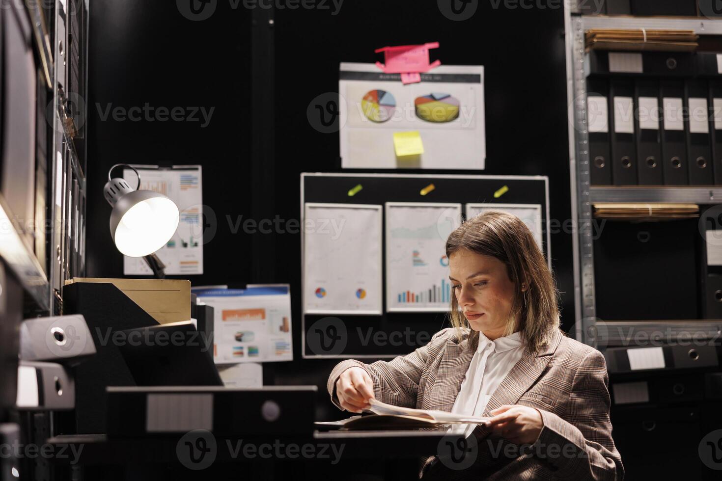 Bookkeeper reading management report in arhive room, working late at night at accountancy research. Corporate employee searching for administrative files. Bureaucracy concept photo