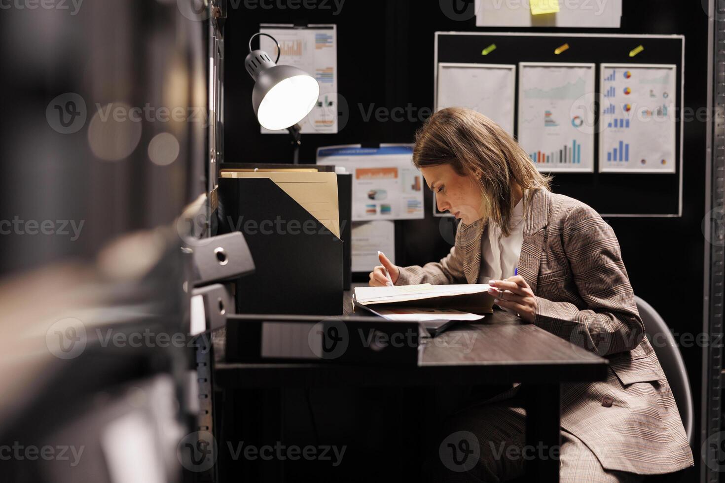 Private detective sitting at desk in arhive room, reading criminology report trying to solve criminal case. Police officer working overtime searching new clues to catch mysterious suspect photo