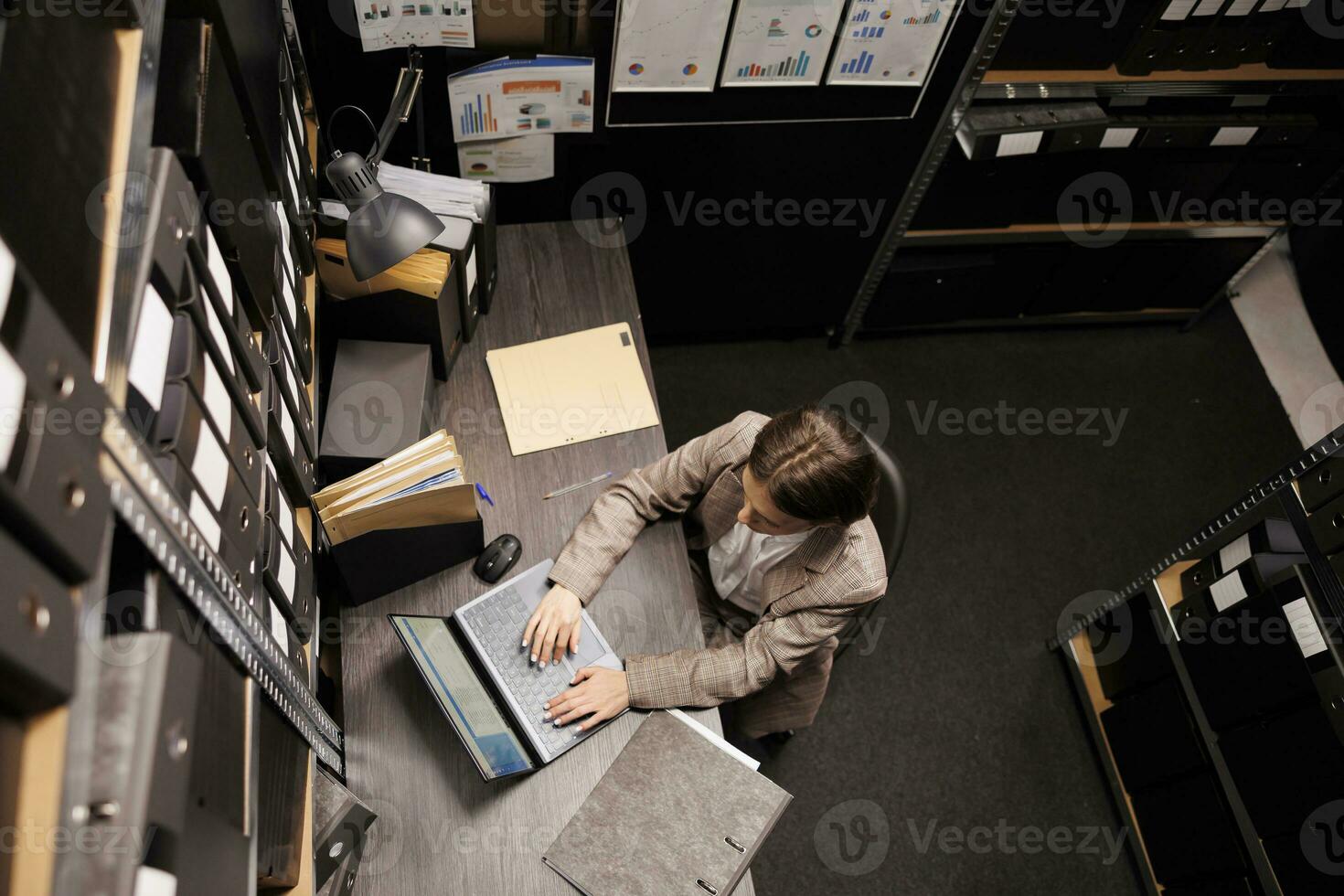 Top view of secretary typing administrative report on laptop computer, analyzing bureaucracy record in arhive room. Businesswoman working late at night at management system. Storage concept photo