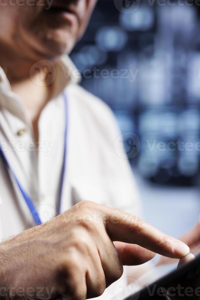 Licensed serviceman inspects server cabinets in data center, ensuring smooth performance. Meticulous repairman monitoring energy consumption across systems components, close up photo