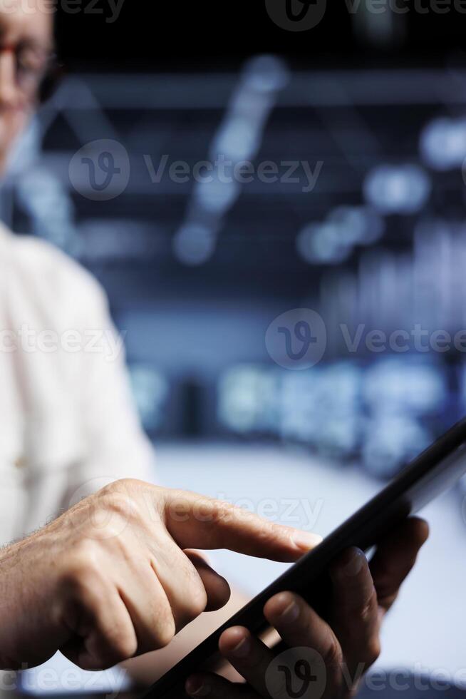 Old IT developer using tablet in high tech facility, installing dedicated VPN servers able to provide encrypted sensitive data, online anonymity and fast speed bandwidth to clients, close up photo